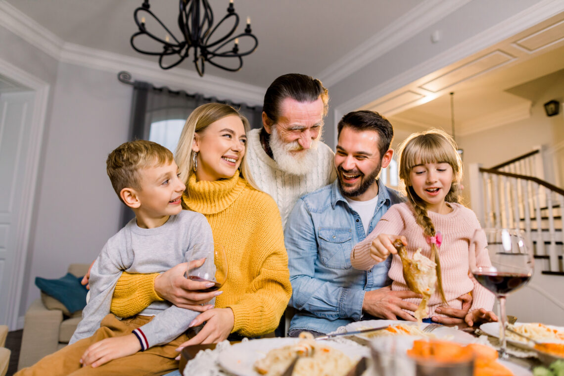 cheerful-grey-haired-grandfather-grandchildren-parents-sitting-table-eating-tasty-yummy-food-having-fun